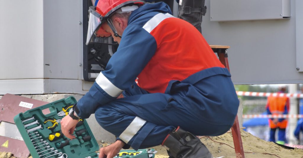 profissional de uniforme azul colete e capacete vermelho estimando os custos de manutenção para aplicar a um equipamento