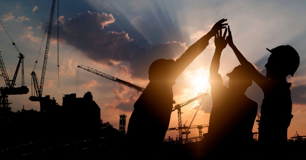 visão da silhueta de 3 homens de uma equipe de obra comemorando com o por do sol ao fundo