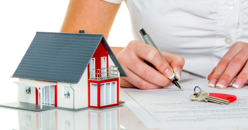 miniatura de casa a frente de uma mulher de camiseta branca assinando um documento de financiamento para construção