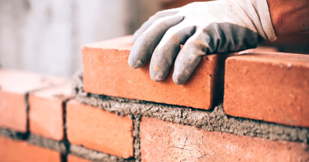 trabalhador de luvas assentando tijolos com cimento mostrando a boa qualidade do material de construção