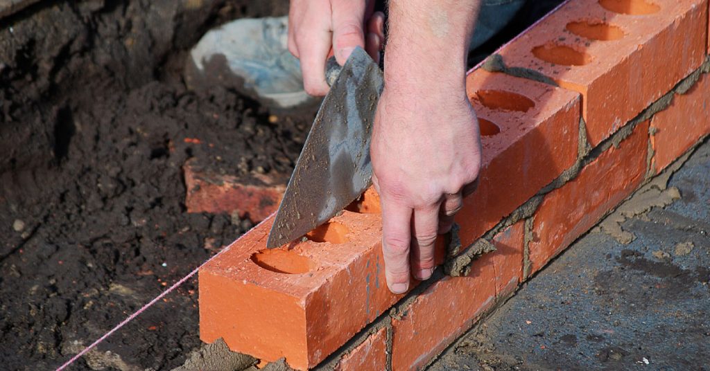 visão das mãos de um profissional de construção com uma pá na mão assentando depois de calcular quantidade de tijolos correta