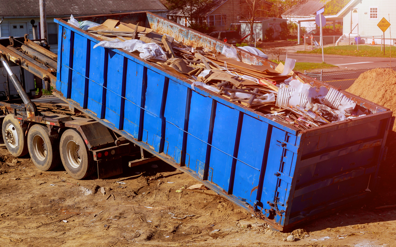 caminhão de caçamba azul descarrega lixo industrial em um terreno em área urbana
